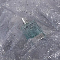 A bottle of LOVALI essential eau de cologne rests on Longan Craft’s Sparkle Glitter Tulle Fabric By The Yard—multicolor, shiny, and delicate tulle ideal for evening gowns—creating a shimmering, elegant backdrop.