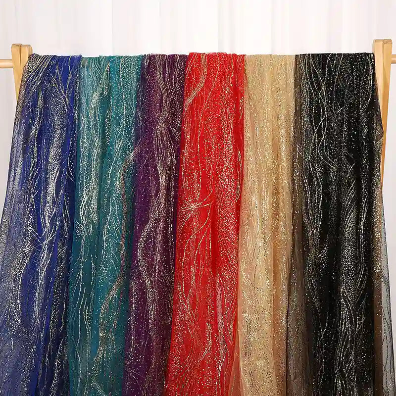 Several sheer, glittery fabrics—ideal for evening gowns—hang side by side. Featured is Longan Craft’s Sparkle Glitter Tulle Fabric By The Yard, a multicolor shimmery tulle available in blue, teal, purple, red, gold, and black.