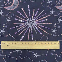 A wooden ruler on Longan Craft’s Star and Moon Sequin Embroidered Tulle Fabric shows the sparkling starburst, crescent moon, constellation, and star design measures about 17 cm wide—ideal for DIY dresses.