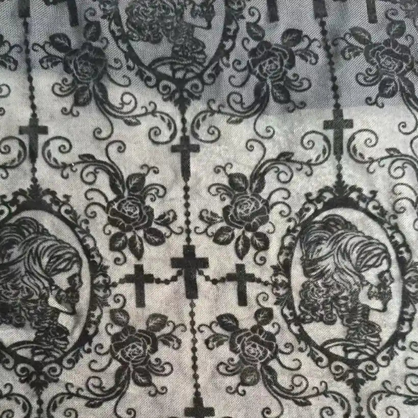 The Stretch Floral Spandex Tulle Fabric by Longan Craft features richly patterned black flocked tulle with gothic-style skeleton cameos, ornate roses, vines, and crosses—perfect for unique dancewear or dressmaking projects.