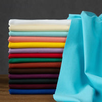 A neatly stacked pile of colorful Longan Craft Cotton Ponte Knit Fabric by the yard rests on a wooden surface, with one light blue elastic double-sided ponte roma cloth draped to the right.