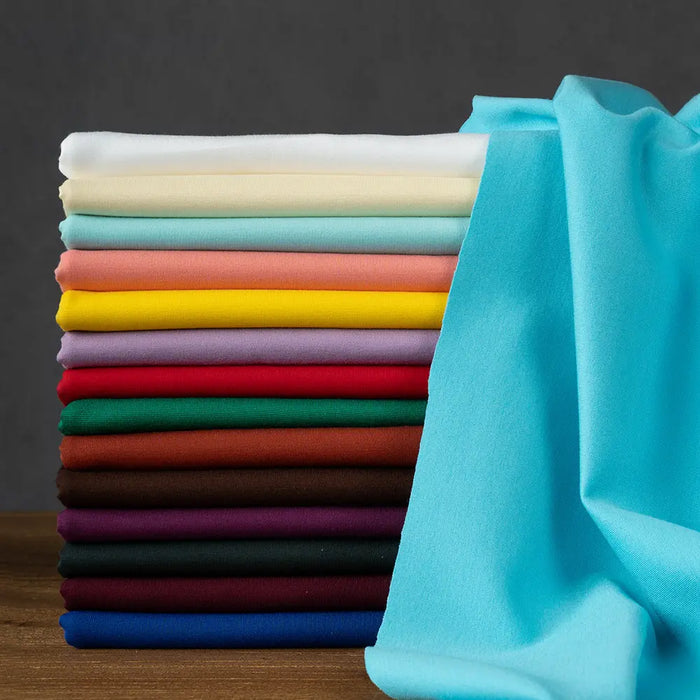 A neatly stacked pile of colorful Longan Craft Cotton Ponte Knit Fabric by the yard rests on a wooden surface, with one light blue elastic double-sided ponte roma cloth draped to the right.