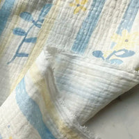 A close-up of Longan Craft’s Striped Floral Print Gauze Fabric By The Yard, made from 100% cotton double gauze material, featuring a textured, breathable weave with soft pastel blue stripes and delicate yellow floral prints. The fabric is slightly folded to display both the front and back sides, highlighting its ideal use for pajamas.
