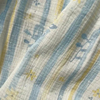 Here’s a rewritten version of the sentence using your product data: A close-up of Longan Craft’s Striped Floral Print Gauze Fabric By The Yard, made from 100% cotton printed double gauze, features vertical blue and yellow stripes accented with delicate floral and leaf patterns. The fabric appears soft, slightly wrinkled, and highlights the breathable texture characteristic of quality double gauze material—perfect for pajamas.