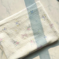 A piece of Longan Craft’s Striped Floral Print Gauze Fabric, made from 100% cotton double gauze and featuring a delicate floral and stripe pattern, lies unfolded on a light marble surface, bathed in soft sunlight and gentle shadows.
