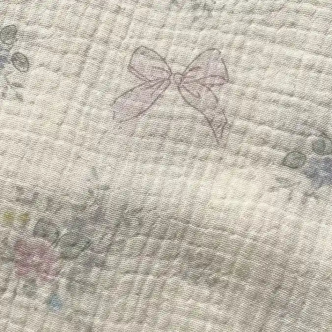 Experience the delicate charm of Longan Craft’s Striped Floral Print Gauze Fabric by the yard—a pale, quilted 100% cotton double gauze material featuring faint pink bows and subtle floral patterns lightly scattered across its surface, perfect for pajamas and cozy projects.