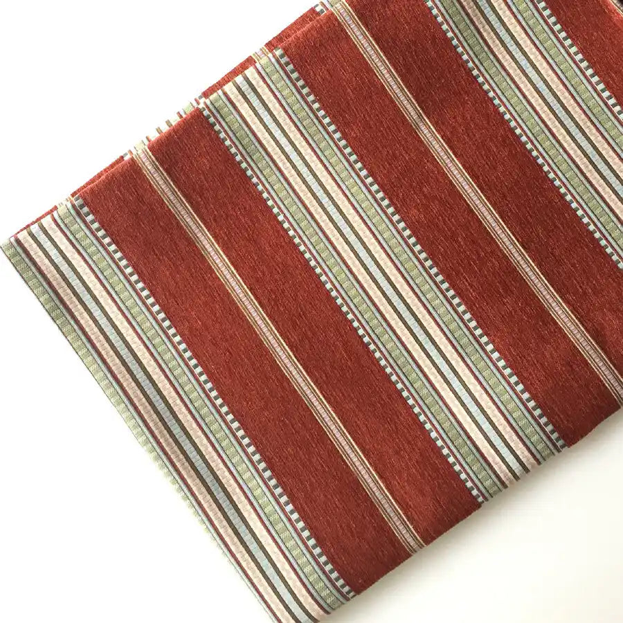 A folded piece of Longan Craft Striped Jacquard Chenille Fabric By The Yard shows wide red and narrow green, white, black, and tan stripes on white—ideal high-quality 100% poly chenille upholstery fabric for cushions or sofas.