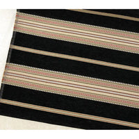 A section of the Longan Craft Striped Jacquard Chenille Fabric By The Yard, featuring wide black and narrow beige stripes with red and tan patterns, is laid on a light floor. This 100% poly chenille upholstery fabric is high-quality and perfect for cushions.