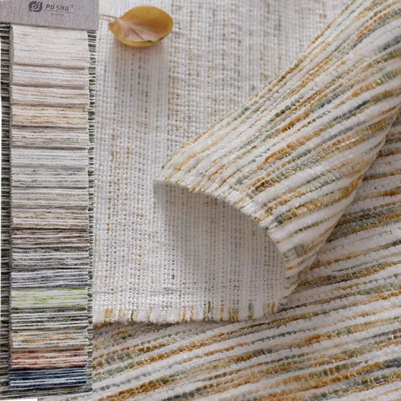 A close-up of Longan Craft's Striped Jacquard Chenille Fabric By The Yard, a colorful and durable poly woven chenille upholstery material, with a fabric sample card to the left and a yellow leaf on top.