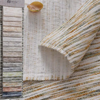 A close-up of Longan Craft's Striped Jacquard Chenille Fabric By The Yard, a colorful and durable poly woven chenille upholstery material, with a fabric sample card to the left and a yellow leaf on top.