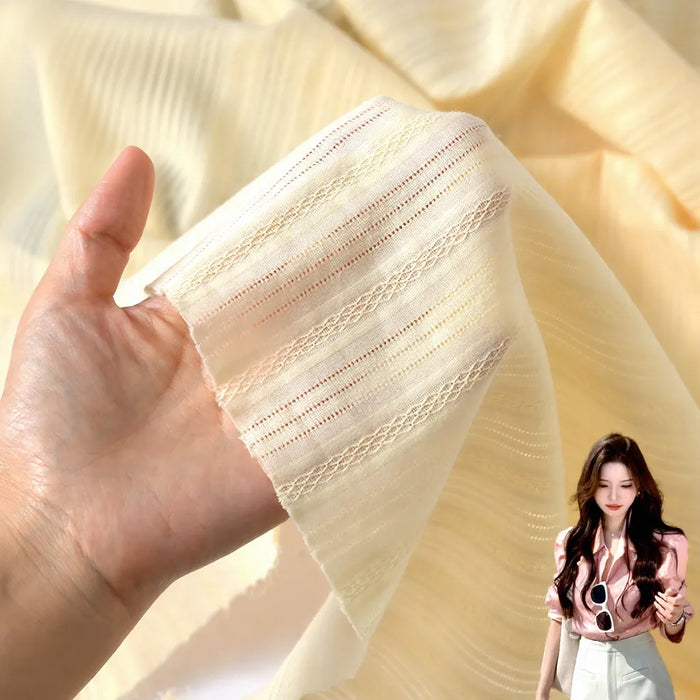 A hand holds Longan Craft’s Striped Openwork Jacquard Dobby Fabric By The Yard, a sheer light yellow cotton perfect for apparel; inset shows a woman in a light pink blouse and white pants.