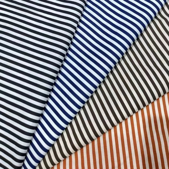 Four pieces of Longan Craft's Striped Print Lawn Fabric By The Yard—pure cotton in black, blue, brown, and orange stripes—are laid diagonally side by side, highlighting the fabric’s classic striped design and soft texture for shirts.