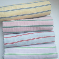 Four rolls of Longan Craft Striped Printed Gauze Fabric By The Yard—yellow/gray, pink/green, blue/red, lavender/green—are stacked horizontally. This double 100% cotton gauze is breathable and perfect for cozy, stylish projects.