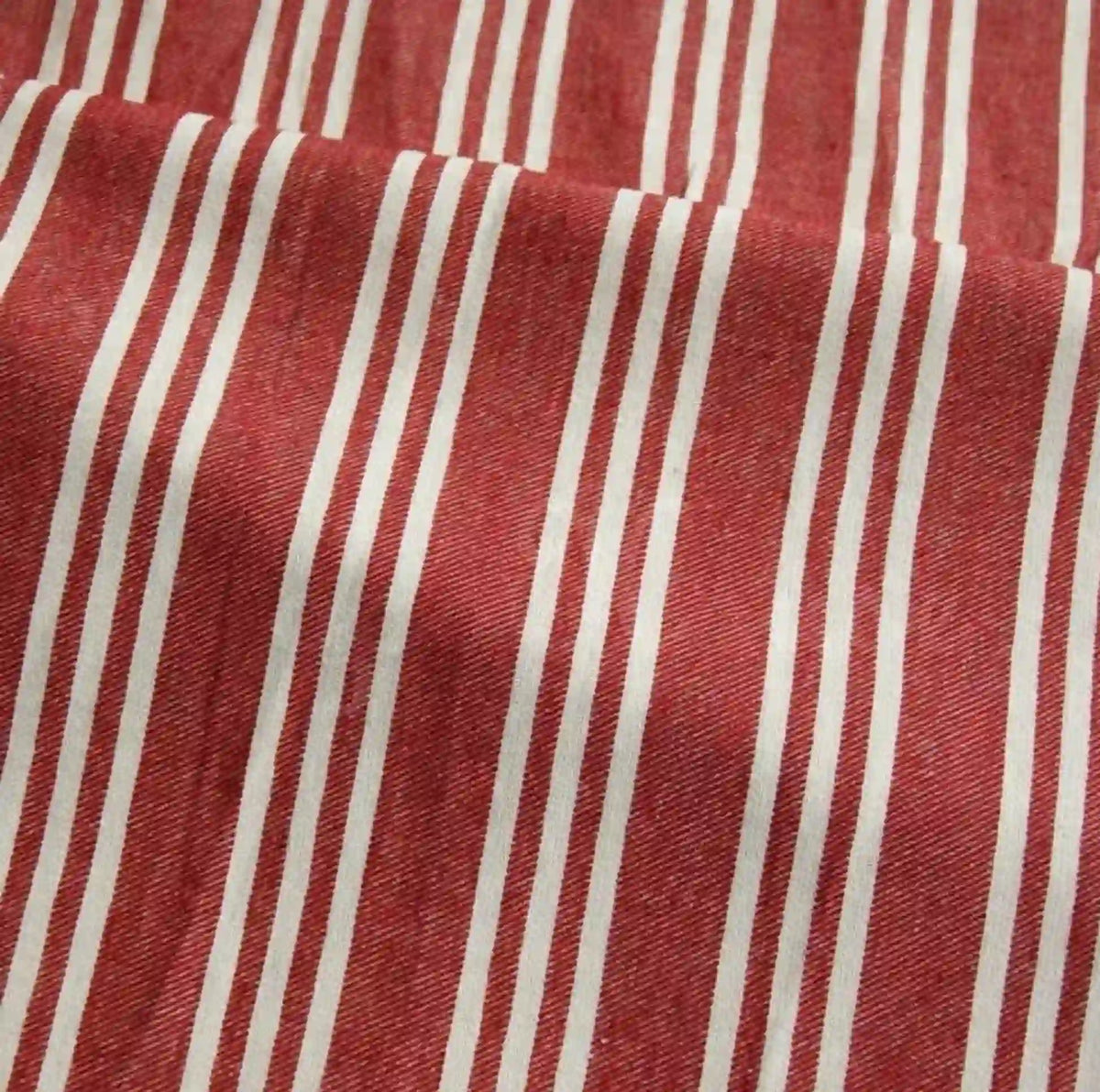 The Striped Printed Linen Fabric By The Yard from Longan Craft is a breathable cotton linen blend fabric featuring a colorful stripe pattern with evenly spaced vertical white stripes of varying widths on a red background. This slightly textured fabric may appear softly wrinkled or folded, making it ideal for dresses and other garment projects.