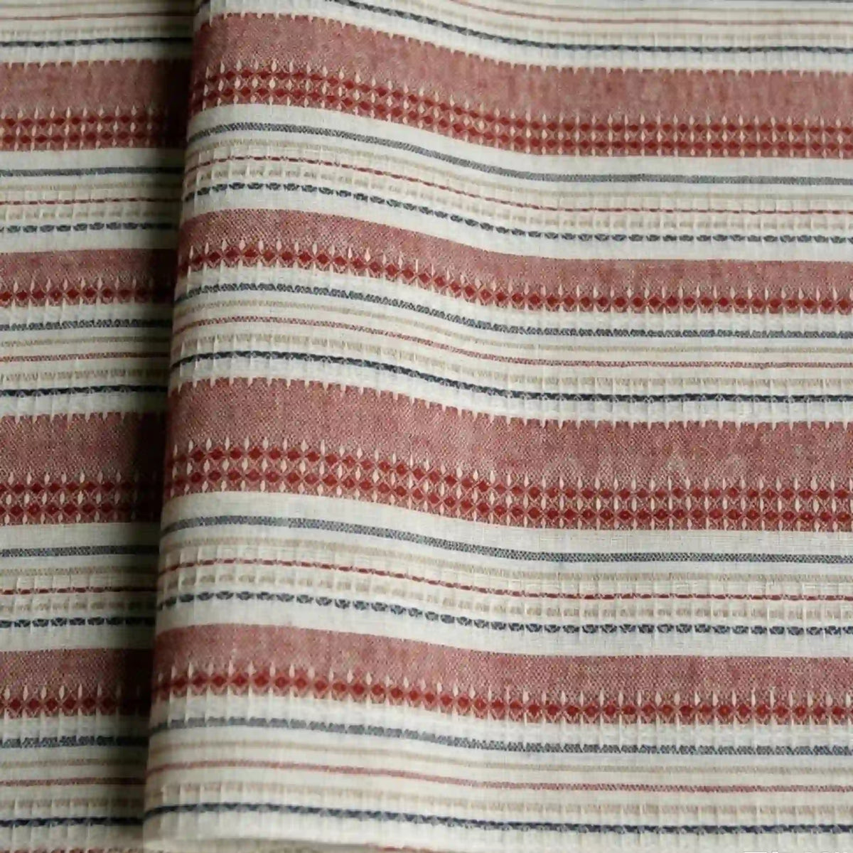 A close-up of Longan Craft’s Striped Printed Linen Fabric By The Yard, a cotton linen blend featuring colorful horizontal stripes in red, white, and blue with small geometric patterns. The breathable fabric is slightly folded, highlighting the texture and detail of the woven material—ideal for dresses.