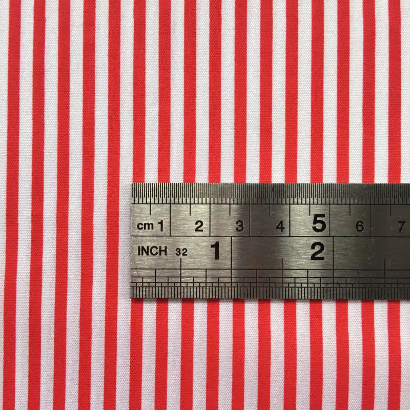 A metal ruler on Longan Craft's Striped Printed Peachskin Fabric By The Yard shows centimeter and inch measurements across evenly spaced red and white stripes. This polyester peachskin material is perfect for DIY clothing projects.