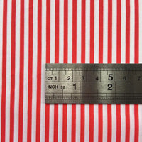 A metal ruler on Longan Craft's Striped Printed Peachskin Fabric By The Yard shows centimeter and inch measurements across evenly spaced red and white stripes. This polyester peachskin material is perfect for DIY clothing projects.