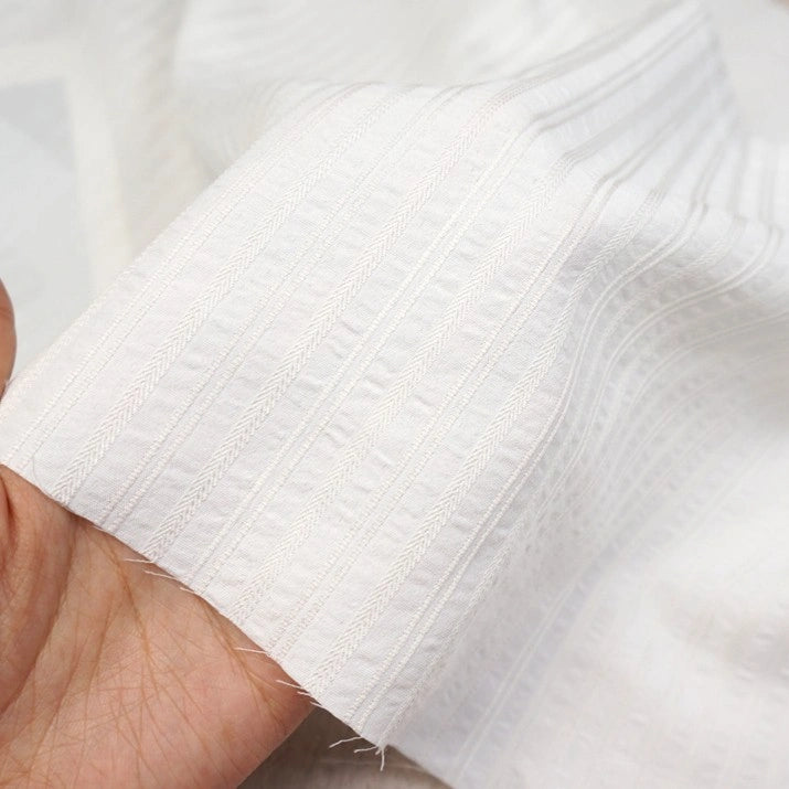 A hand holds Longan Craft’s Striped Rayon Dobby Fabric by the yard, a polyester jacquard dobby material with subtle weave details and soft folds—perfect textile for blouses.