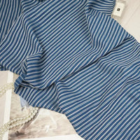 A blue Striped Rayon Dobby Fabric by the yard from Longan Craft, featuring thin white stripes, is elegantly displayed with pearls and a clear perfume bottle on a light surface—ideal jacquard textile for blouses and crafts.