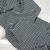 A close-up of Longan Craft Striped Rayon Dobby Fabric By The Yard shows thin white vertical stripes on black polyester jacquard, slightly wrinkled and draped over a light surface, with a strand of pearls partly visible beneath the fabric.