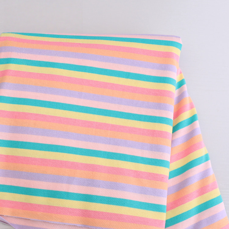 A folded Longan Craft Striped Jersey Fabric By The Yard, a stretchable cotton spandex textile with horizontal pastel yellow, green, pink, and purple stripes, is laid on a light gray surface—perfect for DIY short sleeves.