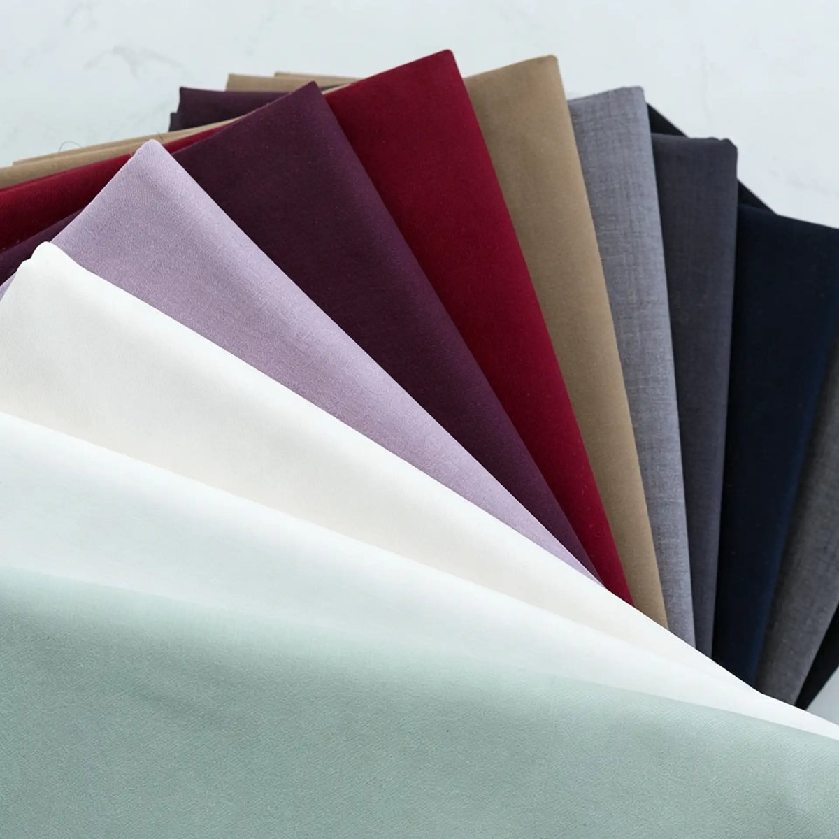 A fan of Thick Cotton Gabardine Fabric by Longan Craft in white, mint green, lavender, and burgundy is displayed on a light surface, showcasing this durable twill material ideal for uniforms.