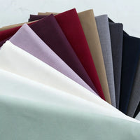 A fan of Thick Cotton Gabardine Fabric by Longan Craft in white, mint green, lavender, and burgundy is displayed on a light surface, showcasing this durable twill material ideal for uniforms.