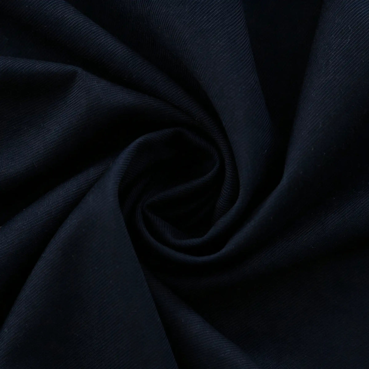 Close-up of Longan Craft Thick Cotton Gabardine Fabric by the Yard in navy blue, twisted to show its smooth, subtly textured, heavyweight cotton-polyester twill—an ideal material for uniforms with a soft feel and gentle sheen.