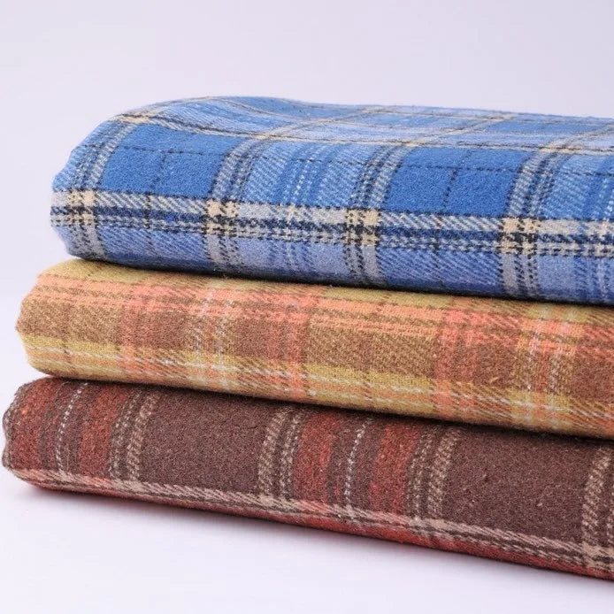 Three folded blankets made from Longan Craft’s Thick Plaid Mammoth Flannel Fabric are stacked atop one another, each showcasing classic heavyweight cotton brushed flannel patterns in blue, yellow, and brown against a simple light background.
