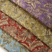 Four rolls of Longan Craft’s Thick Viscose Chenille Fabric By The Yard in purple, green, red, and blue with gold and beige botanical jacquard patterns are stacked diagonally. Ideal for durable draperies and luxurious upholstery projects.