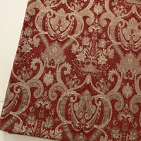 Longan Craft’s Thick Viscose Chenille Fabric By The Yard features a durable, ornate gold and beige botanical damask on deep red. This jacquard chenille material is draped at an angle on a light surface—ideal for upholstery or draperies.