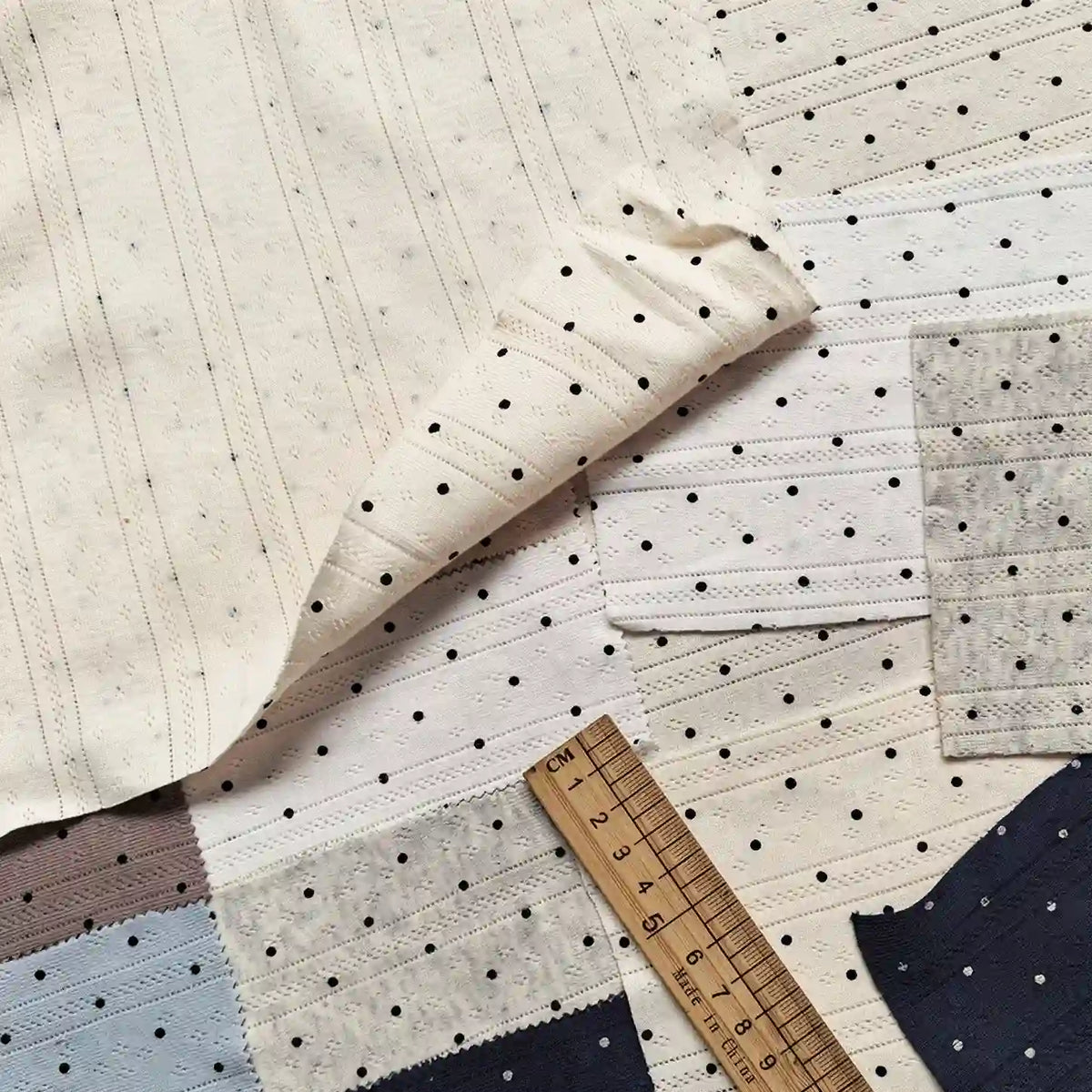 Samples of Tiny Polka Dot Print Pointelle Fabric By The Yard in various colors featuring a ribbed texture and tiny polka dot patterns, shown with a wooden ruler for scale.