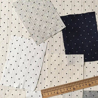Four swatches of Tiny Polka Dot Print Pointelle Fabric By The Yard in white, cream, and navy polka dot patterns arranged near a wooden ruler.