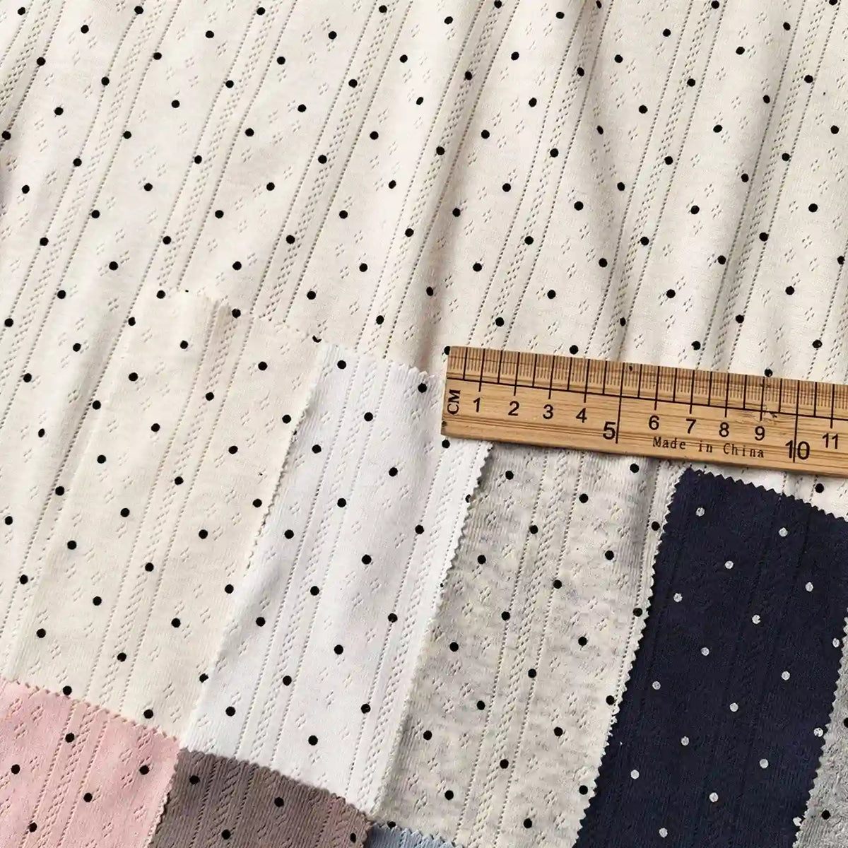 Swatches of Tiny Polka Dot Print Pointelle Fabric By The Yard in various colors, featuring a ribbed texture and a tiny polka dot pattern, with a wooden ruler across the top for scale.