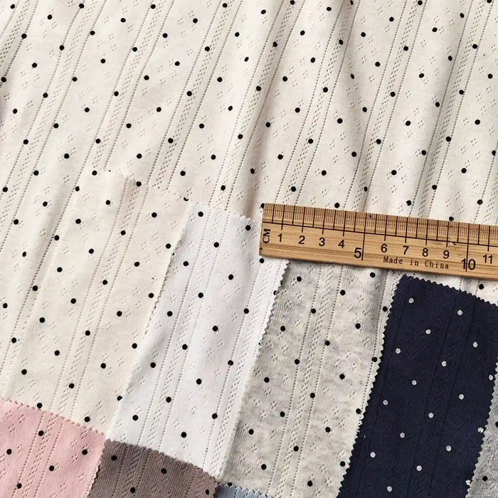 Swatches of Tiny Polka Dot Print Pointelle Fabric By The Yard in various colors, featuring a ribbed texture and a tiny polka dot pattern, with a wooden ruler across the top for scale.