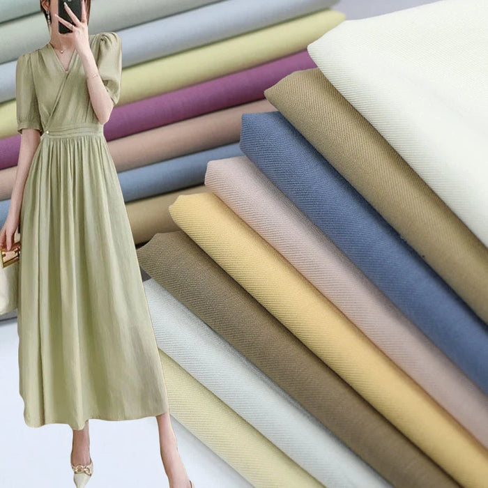 A woman in a light green dress stands by stacks of Longan Craft Twill Cotton Lyocell Fabric in comfy, breathable pastel and neutral colors—blue, yellow, beige, pink, and white—ideal for shirts.