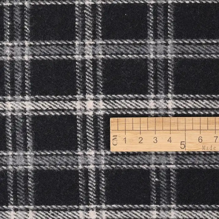 A wooden ruler rests on the Longan Craft Vintage Checked Mammoth Flannel Fabric, aligning its 5 cm mark with a horizontal stripe to showcase the classic black and white thick cotton gingham pattern of this heavyweight flannelette sewing material.
