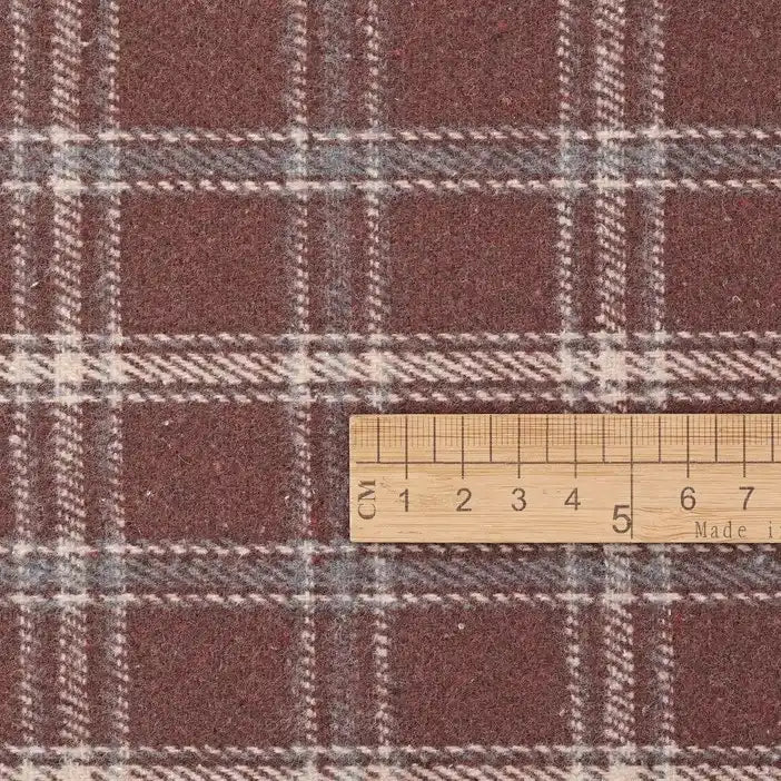 A wooden ruler, displaying centimeter measurements, is placed on Longan Craft’s Vintage Checked Mammoth Flannel Fabric by the yard—a thick cotton gingham flannelette in a maroon and white check pattern.