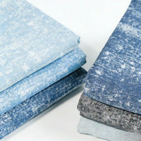 Two stacks of Longan Craft Washed Denim Fabric By The Yard, premium vintage cotton denim cloth in blue and gray tones with a textured, mottled look, are neatly folded on a white surface.