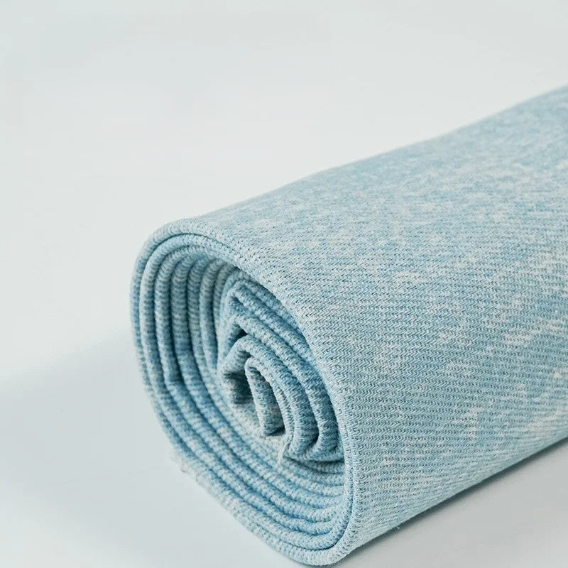 A close-up of Longan Craft's Washed Denim Fabric By The Yard, a premium soft vintage cotton denim textile for jeans, rolled up to showcase its textured light blue appearance on a white surface.