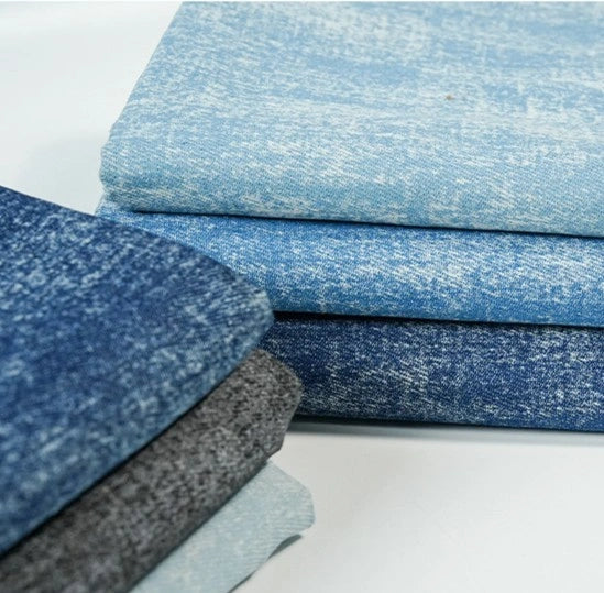 Stacks of Longan Craft Washed Denim Fabric By The Yard in blue and gray shades, with a textured, vintage look, are neatly arranged on a white surface—premium soft cotton denim perfect for jeans and craft projects.
