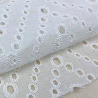 Close-up of Longan Craft's White Floral Eyelet Embroidered Voile Fabric By The Yard, made from 100% cotton with hollow out embroidery. This airy sewing fabric is ideal for dressmaking and showcases intricate, repeating floral designs.
