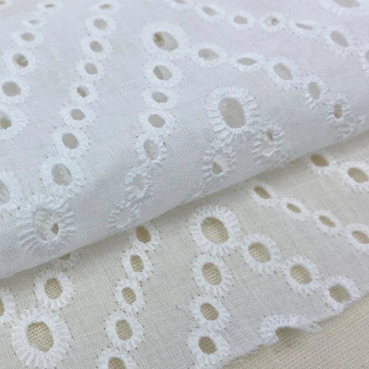 Close-up of Longan Craft's White Floral Eyelet Embroidered Voile Fabric By The Yard, made from 100% cotton with hollow out embroidery. This airy sewing fabric is ideal for dressmaking and showcases intricate, repeating floral designs.