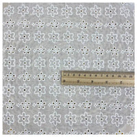 The Longan Craft White Floral Eyelet Embroidered Voile Fabric by the yard is a lightweight, breathable 100% cotton material in light gray with white floral hollow-out embroidery. A wooden ruler in centimeters and inches shows the scale on the fabric.