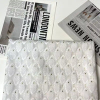 Longan Craft’s White Leaf Pattern Organza Fabric By The Yard, a botanical jacquard material for clothing, is displayed on a white surface with newspaper sheets adorned with bold headlines and fashion images.