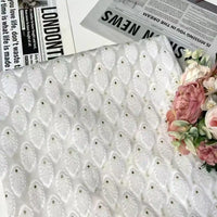 The White Leaf Pattern Organza Fabric by Longan Craft is displayed on a table beside pink flowers and newspapers, including one with the headline "LONDON THE." This botanical jacquard organza is perfect for clothing projects.