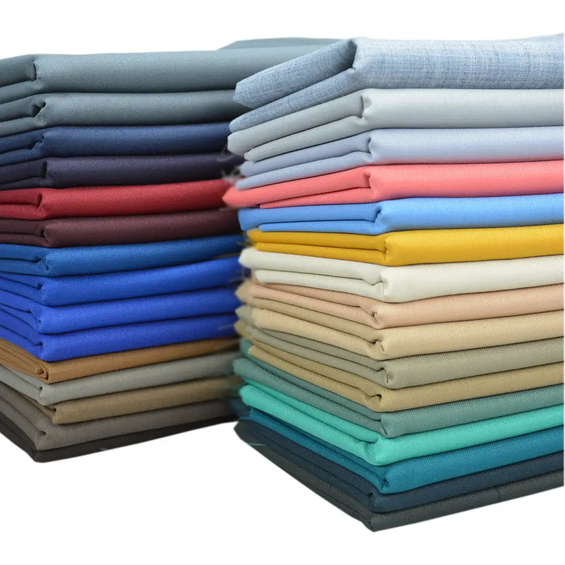 Stacks of Longan raft Worsted Wool Gabardine Fabric By The Yard in assorted colors—blue, gray, red, yellow, tan, green, and beige—are arranged in two piles against a white background. Perfect for tailored suits and crafted from durable poly wool blend.