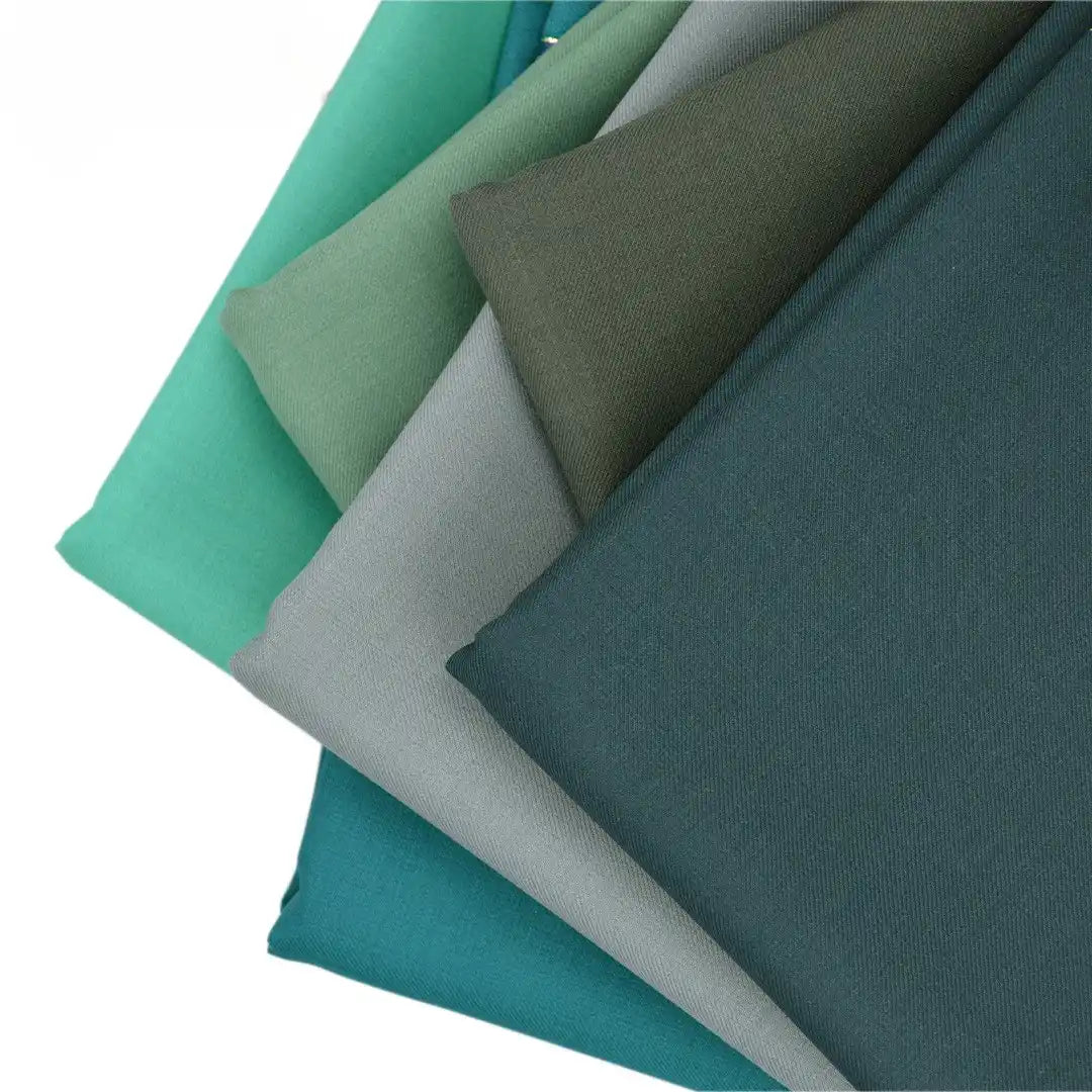 Five neatly stacked pieces of Longan raft Worsted Wool Gabardine Fabric in green and teal shades, displayed in a fan on white. Durable colorful poly wool twill gabardine—ideal for tailored suits, available by the yard.