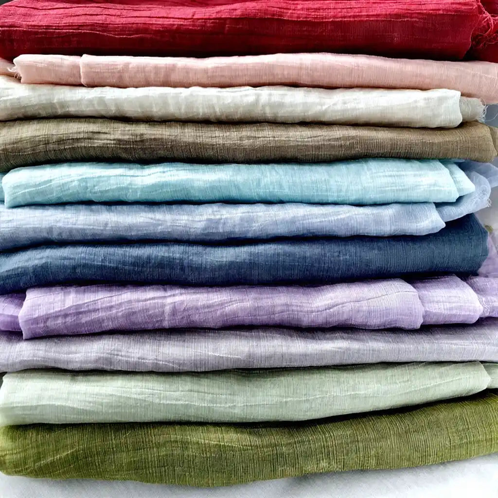 A gradient stack of Longan Craft’s sustainable Wrinkled Lyocell Fabrics showcases red, pink, white, brown, blue, purple, and green solids—versatile breathable textiles by the yard for stylish tops.