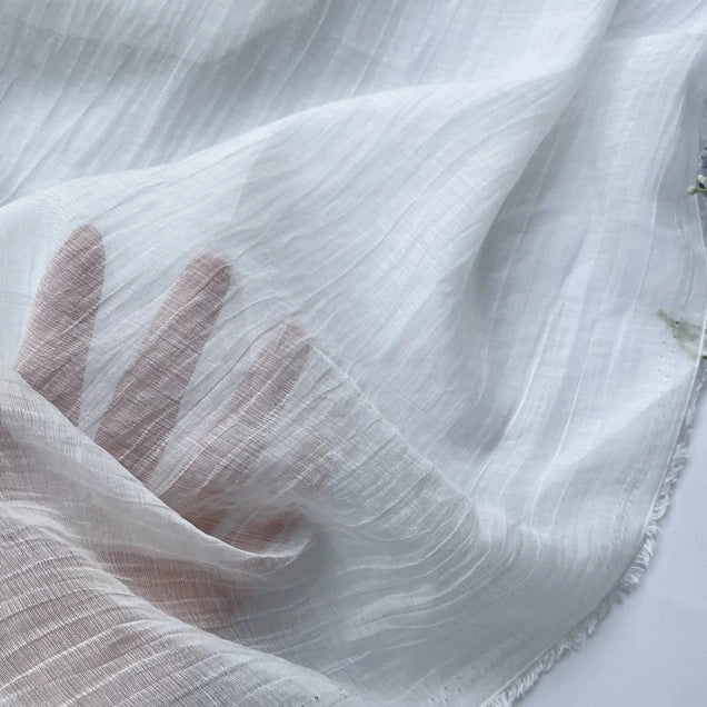 A hand is pressed against Longan Craft's Wrinkled Lyocell Fabric By The Yard, a breathable, sheer white sustainable textile with subtle stripes and soft folds, revealing fingers through its lightweight material—perfect for tops.